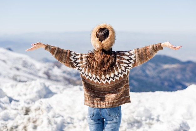 空に照らして雪の上に腕を伸ばしたまま立っている女性の後ろの景色