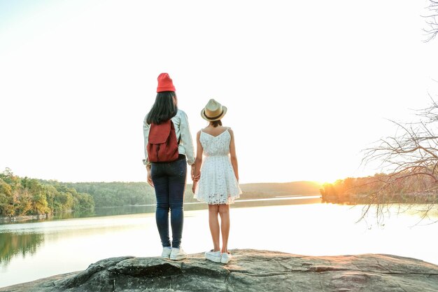 Photo rear view of woman standing with daughter on rock by lake against clear sky