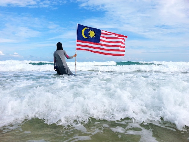 空の向こうの海にマレーシアの旗を掲げている女性の後ろの景色