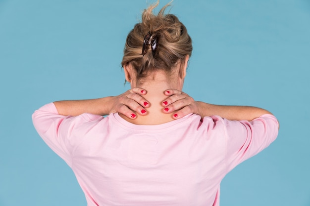 Rear view of woman suffering from neck pain against blue wallpaper