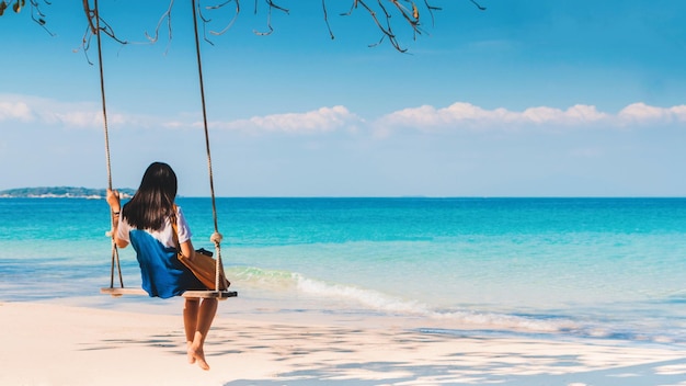 Rear view of woman on swing at beach against sky