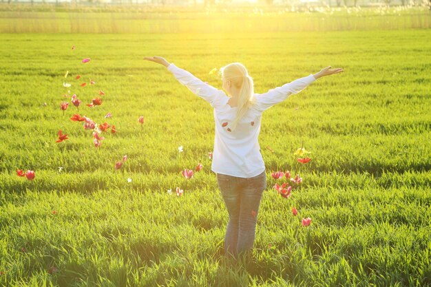 晴れた日に草原に立って花を投げる女性の後ろの景色