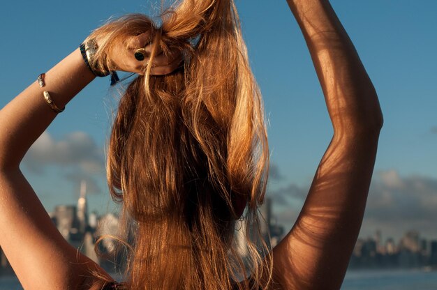 Foto vista posteriore di una donna che lega i capelli biondi sulla spiaggia contro il cielo durante il tramonto