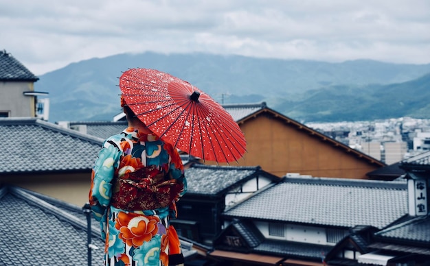 都市の家の屋根のそばに立っている傘の下の女性の後ろの景色