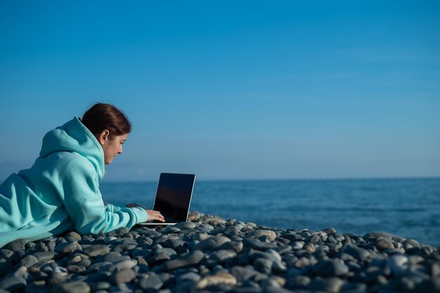 Rear view of woman using mobile phone at beach against clear sky