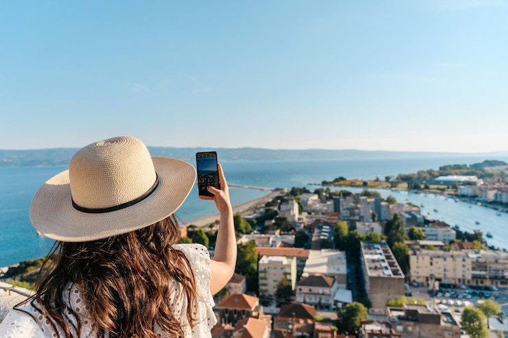 Photo rear view of woman using mobile phone taking photos of beautiful seaside town of omis in croatia