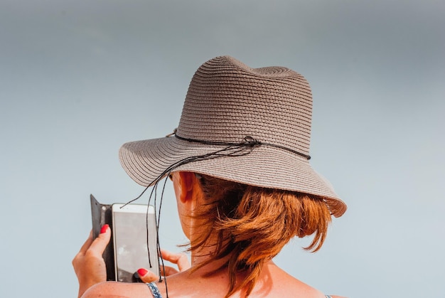 Foto vista posteriore di una donna che usa uno smartphone contro un cielo limpido