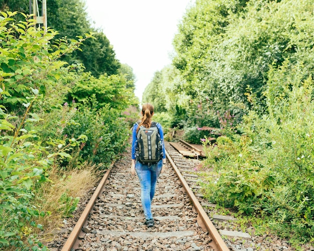 rear view of woman walking on abandoned railroad track amidst plants