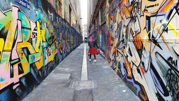 Rear view of woman walking at alley amidst graffiti wall in city