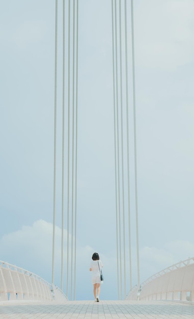 Rear view of woman walking on bridge against sky