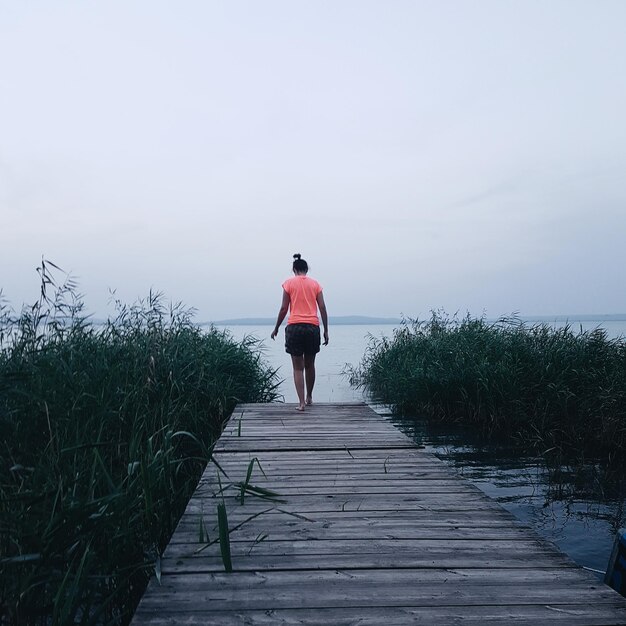 Rear view of woman walking by sea against sky