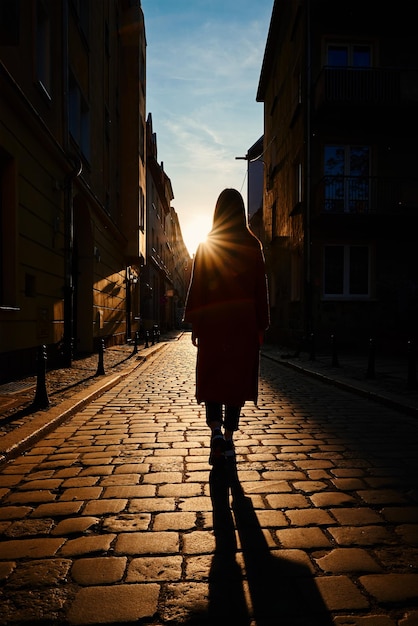 Rear view of woman walking at city street with sunset