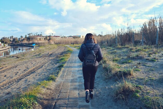 Rear view of woman walking on field against sky