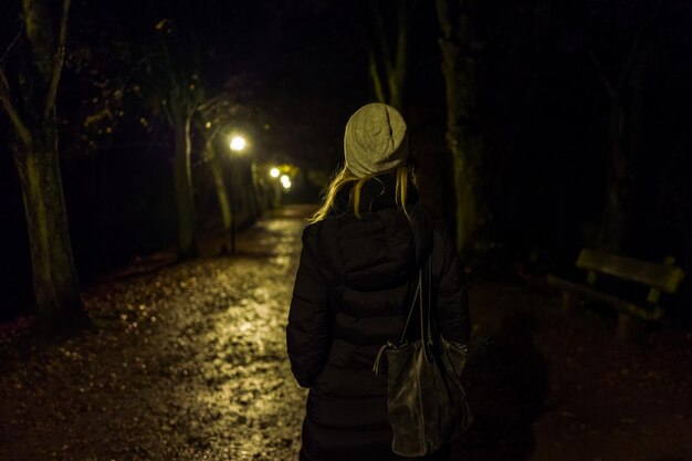 Foto vista posteriore di una donna che cammina su una strada illuminata di notte