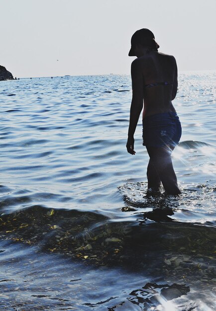 Foto vista posteriore di una donna che cammina nel mare contro il cielo