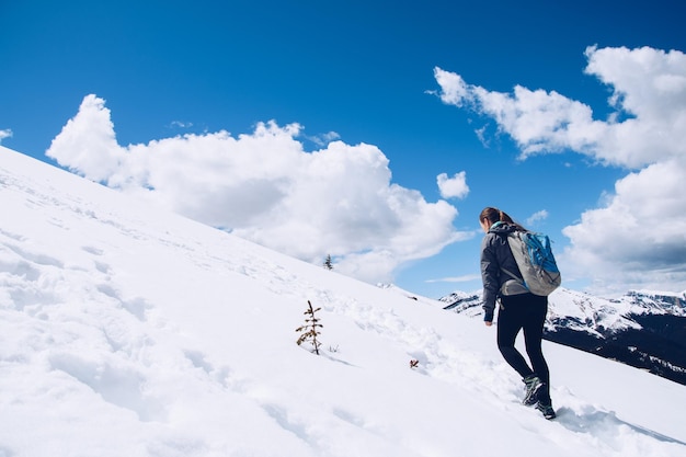 空に向かって雪で覆われた山を歩く女性の後ろの景色