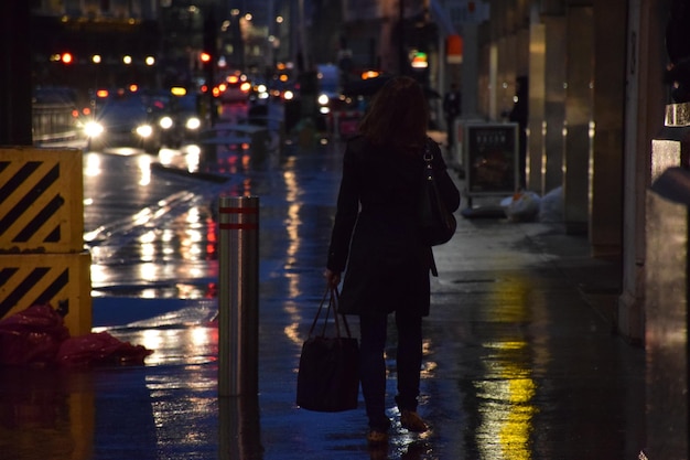 Foto vista posteriore di una donna che cammina sul marciapiede bagnato in città di notte