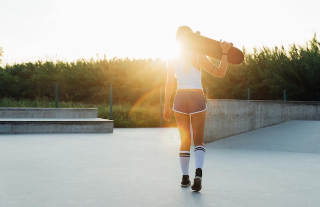 Photo rear view of woman walking with skateboard in park