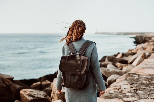 rear view of woman wearing backpack while standing on pier over sea against clear sky
