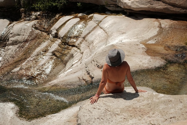 Foto vista posteriore di una donna che indossa un bikini mentre è seduta su una roccia