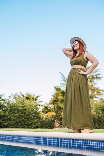 Rear view of woman wearing hat standing against swimming pool against clear sky