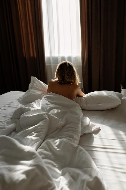 Photo rear view of a woman wearing lingerie and lying on a bed while looking at a window