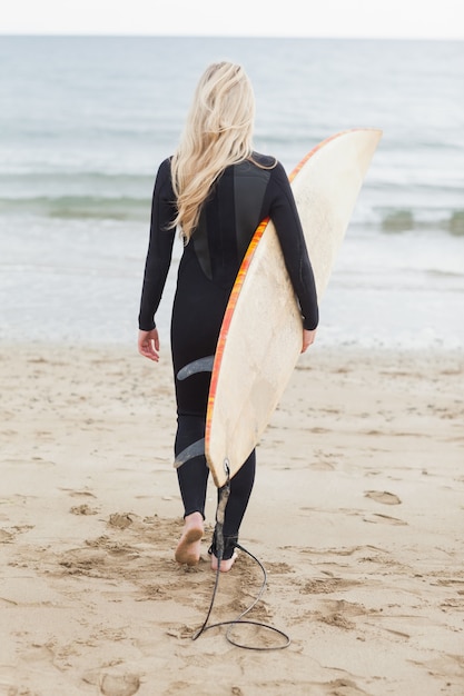 Rear view of a woman in wet suit holding surfboard at beach