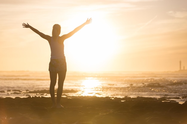 Rear view of woman with arms outstretched at beach during sunset