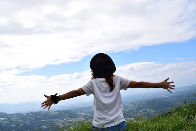 Photo rear view of woman with arms outstretched on grassy hill against cloudy sky