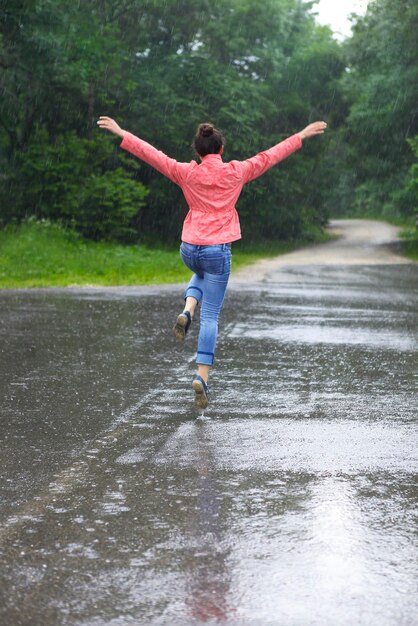 Photo rear view of woman with arms outstretched jumping on road during rainfall