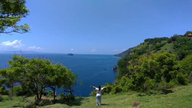 Photo rear view of woman with arms outstretched looking at sea against blue sky