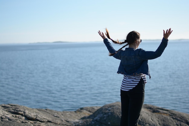 Foto vista posteriore di una donna con le braccia tese guardando il mare contro il cielo