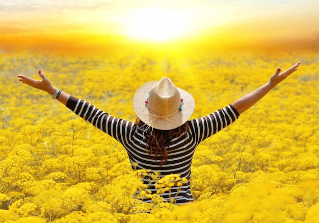 Photo rear view of woman with arms outstretched standing amidst flowers on field during sunset