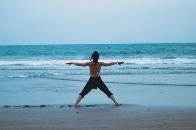 Rear view of woman with arms outstretched standing at beach against clear sky