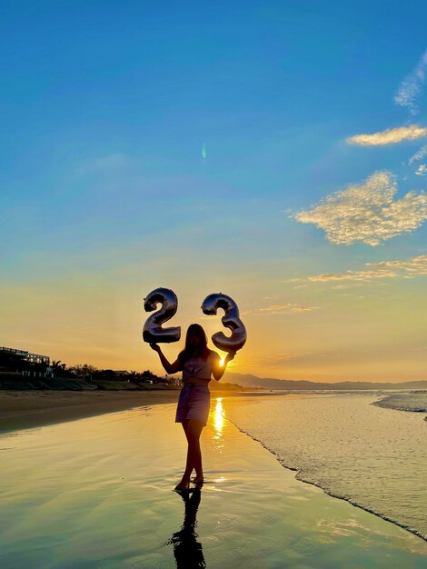 Foto vista posteriore di una donna con le braccia allungate in piedi sulla spiaggia contro il cielo durante il tramonto