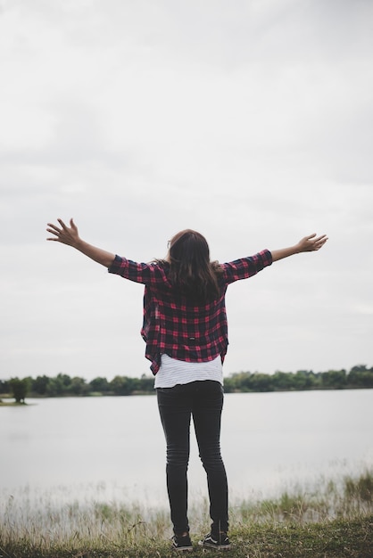 Rear view of woman with arms outstretched standing by lake on field