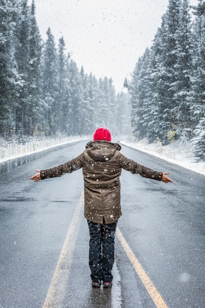 Photo rear view of woman with arms outstretched standing on road during snowfall