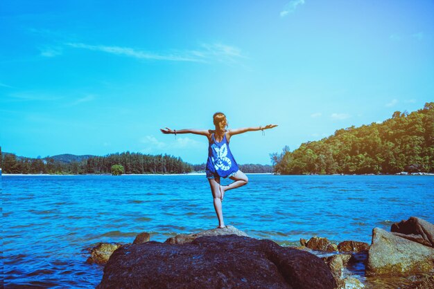 Rear view of woman with arms outstretched standing on rock against sky