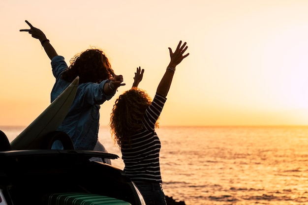 Rear view of woman with arms raised against sea during sunset