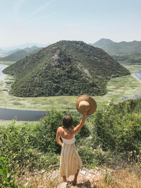 Photo rear view of woman with arms raised holding hat on land