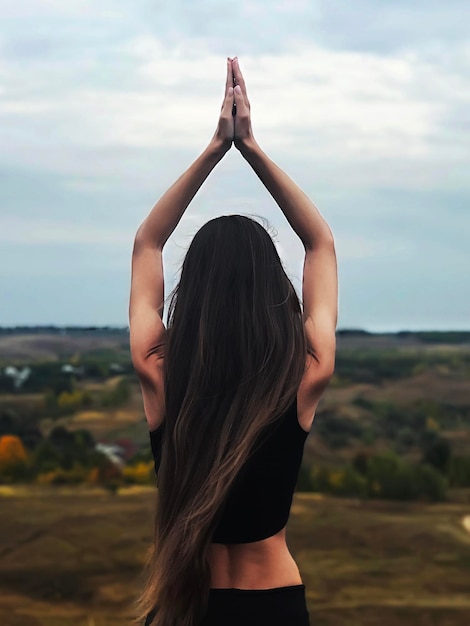 Photo rear view of woman with arms raised meditating against sky