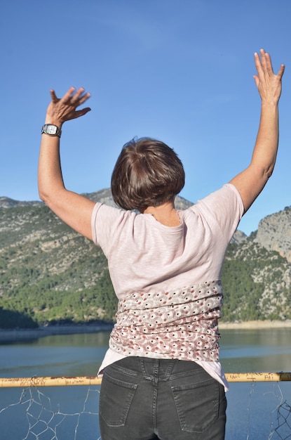 호수 와 산 에 맞서 서 있는 팔 을 들고 있는 여자 의 뒷면