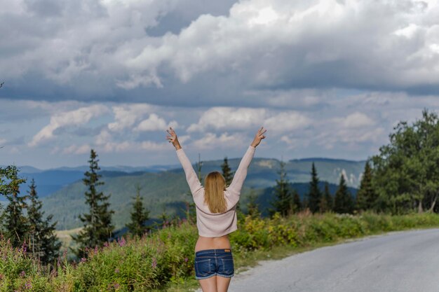 Photo rear view of woman with arms raised standing on mountain road against cloudy sky