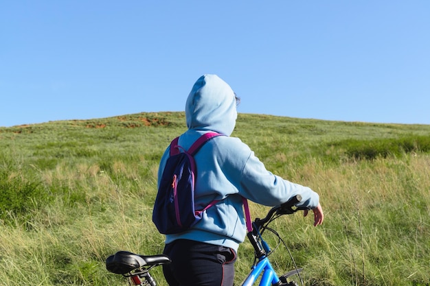 Photo rear view of a woman with a backpack going uphill with a bike, copy space.
