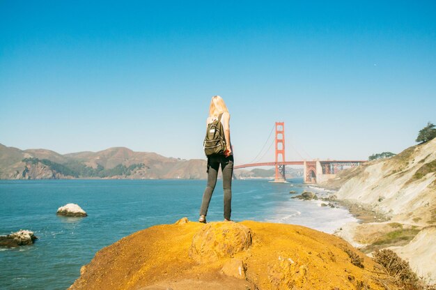 Foto vista posteriore di una donna con uno zaino che guarda il golden gate bridge contro il cielo