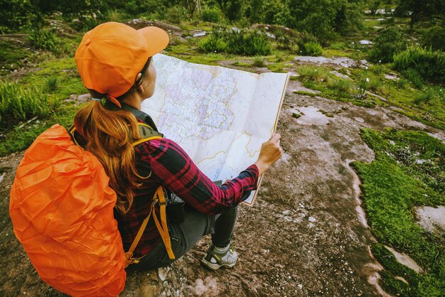 Photo rear view of woman with backpack reading map while sitting on land