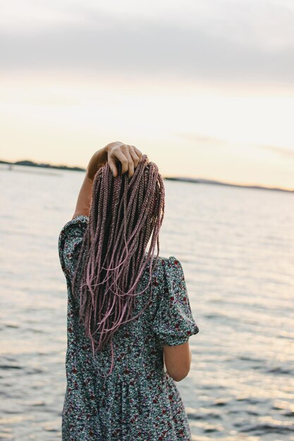 Rear view of woman with hand in hair standing at beach against sky