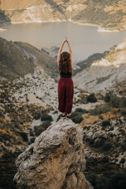 Foto vista posteriore di una donna con le mani giunte in piedi su una formazione rocciosa