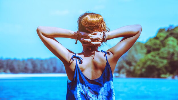 Rear view of woman with hands behind head while standing at beach