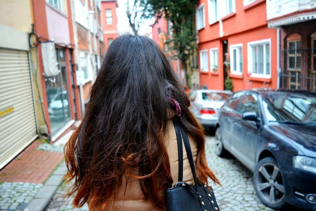 Rear view of woman with long hair by car on street in city